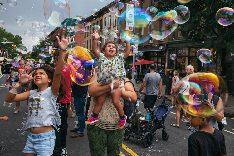 Members of the Park Slope community on the street playing with bubbles.
